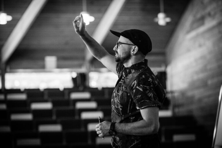 Kingsley gives instruction using his hands to illustrate a point with lights hanging in the background.